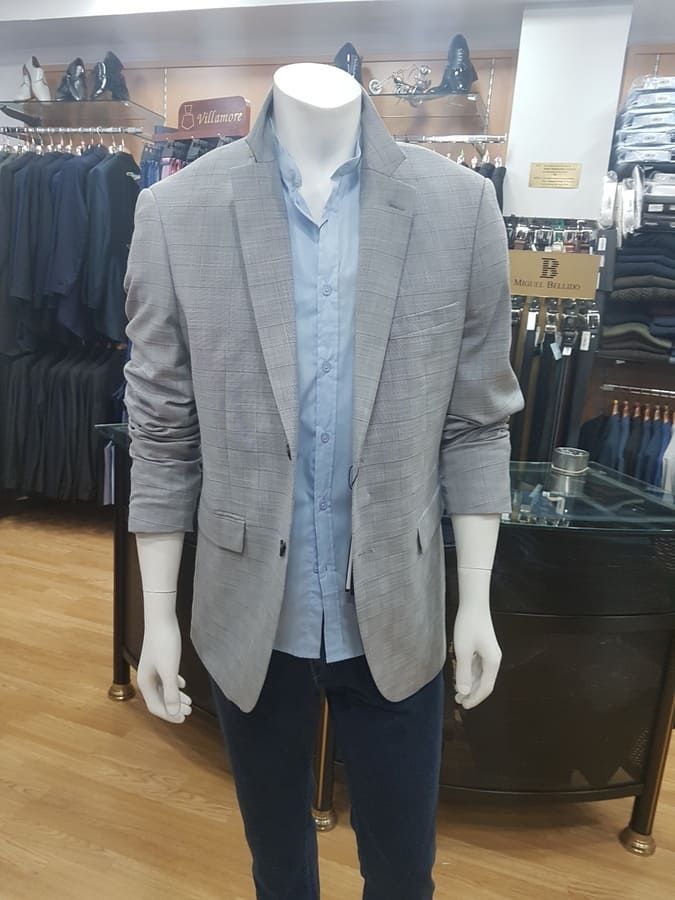Maniquí con blazer gris, camisa azul y jeans oscuros, en una tienda de ropa.