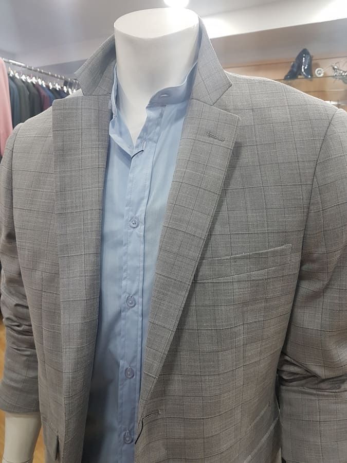 Maniquí con un blazer a cuadros gris sobre una camisa de vestir azul claro.