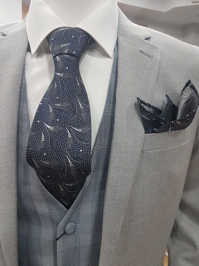 Maniquí con traje gris claro, corbata azul marino con estampado blanco y pañuelo de bolsillo.