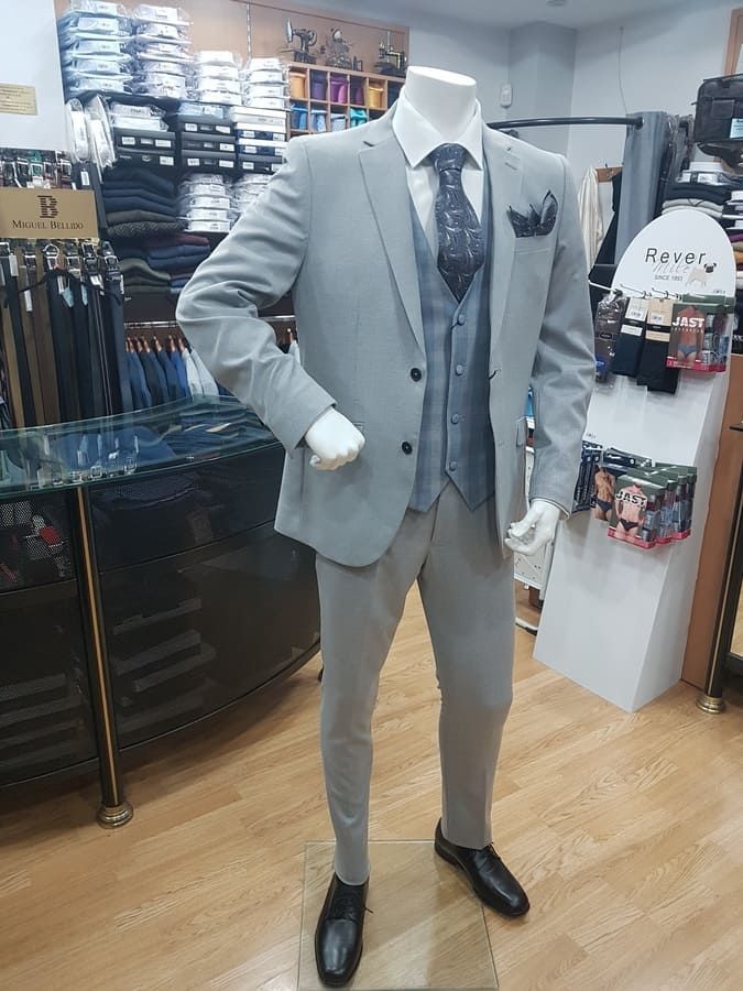 Maniquí con traje gris claro, chaleco y corbata, de pie en una tienda de ropa.