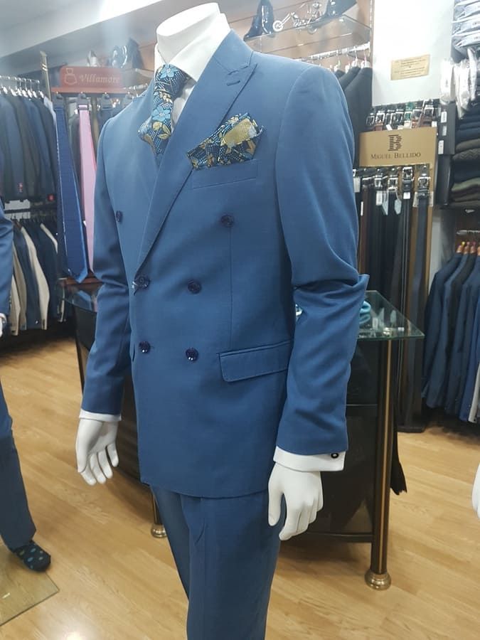 Traje cruzado azul sobre un maniquí con corbata floral y pañuelo de bolsillo en una tienda de ropa.