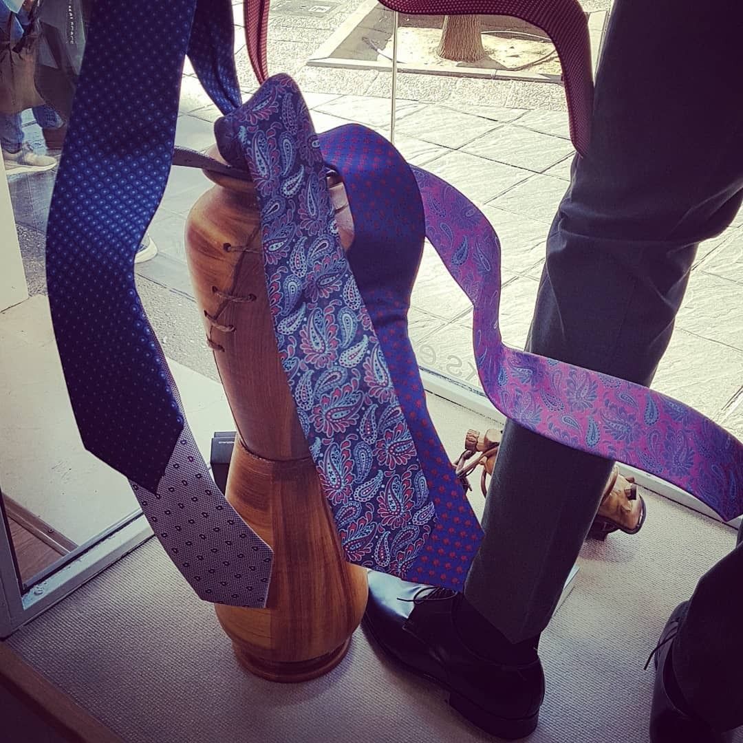 Exhibición de corbatas de colores en un maniquí de madera y una persona que viste zapatos y pantalones negros cerca de una tienda.