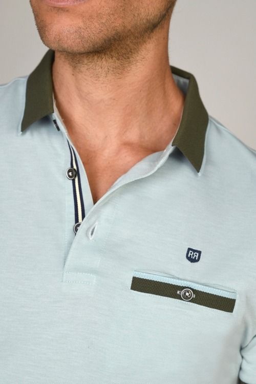 Hombre que viste un polo azul claro con cuello y bolsillo verde oliva.