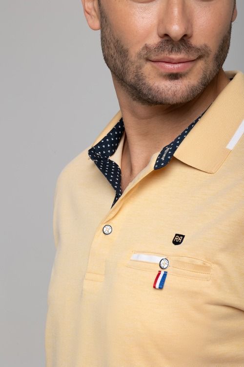 Hombre con polo amarillo, sonriendo. La camisa tiene cuello y bolsillo con lunares azules.