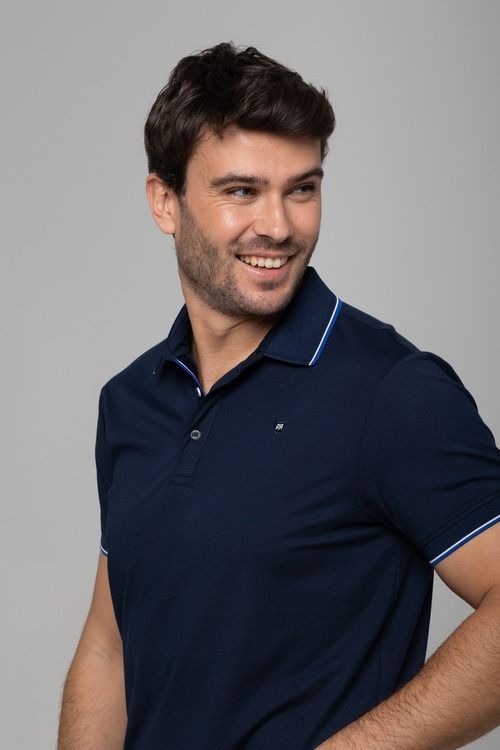 Un hombre con un polo azul marino sonríe y mira por encima del hombro.