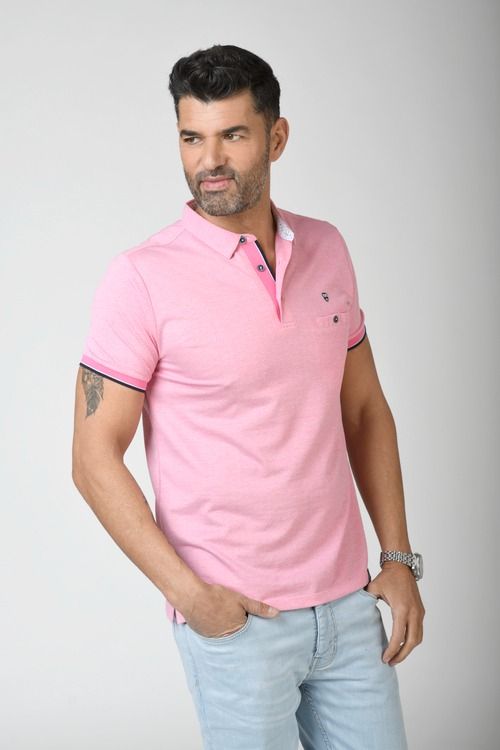 Hombre con polo rosa, jeans azul claro, mirando por encima del hombro y con la mano en el bolsillo.