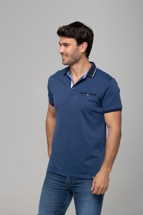 Un hombre con camisa polo azul y pantalones vaqueros sonríe y mira hacia un lado.