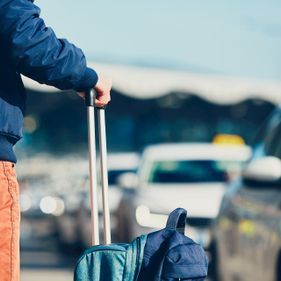 Une personne portant une valise près de voitures, probablement dans un aéroport.