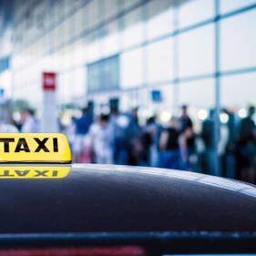Panneau jaune de taxi sur le toit d'une voiture, arrière-plan flou d'un terminal d'aéroport.