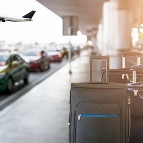 Des valises alignées sur le trottoir de l'aéroport, un avion qui décolle, des voitures qui attendent.