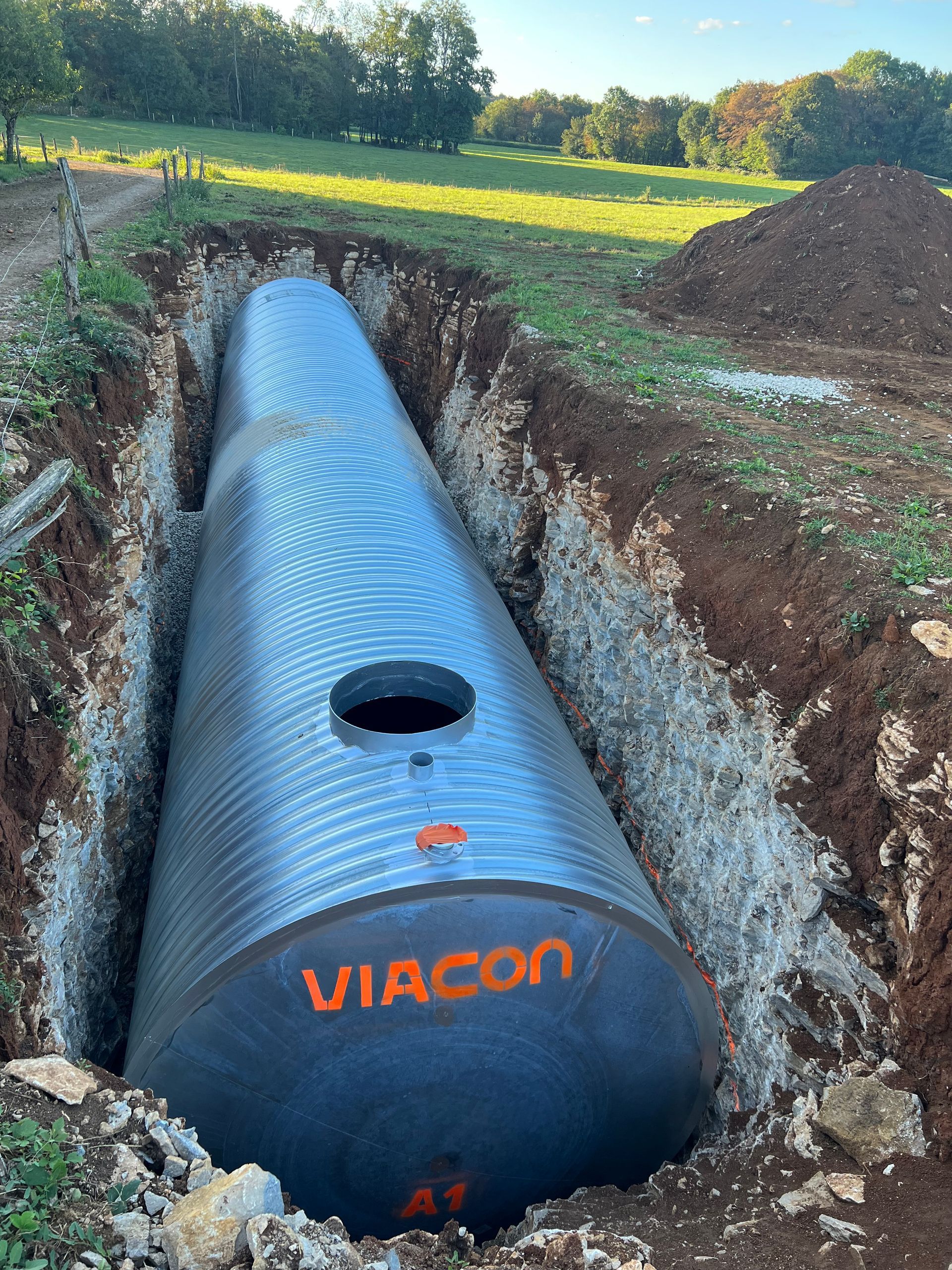 Grand réservoir cylindrique noir, estampillé VIACON, dans une tranchée à l'extérieur.
