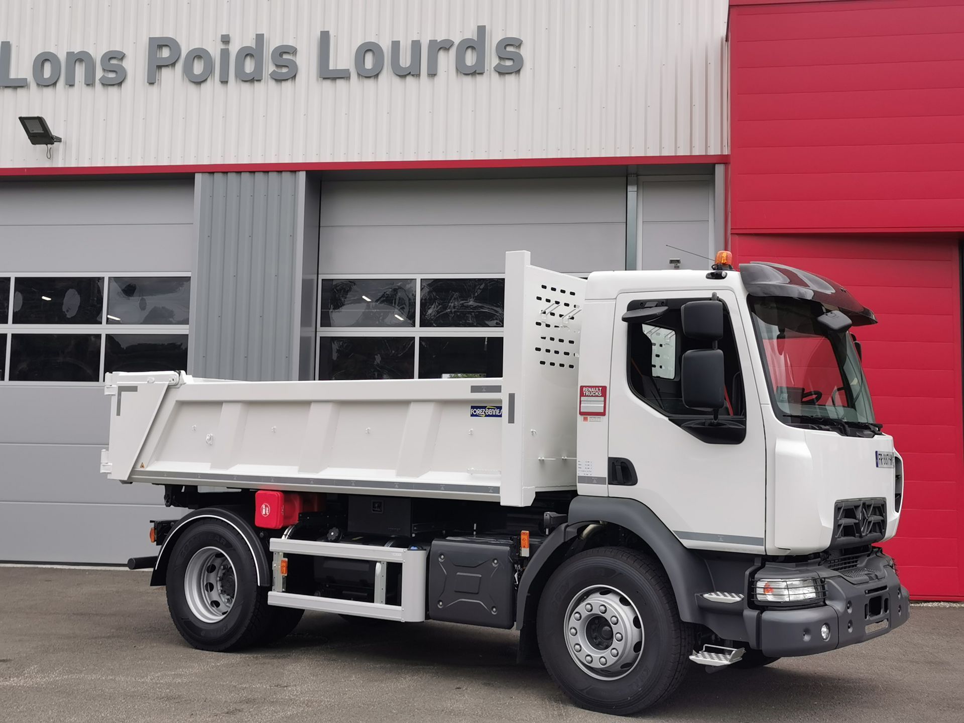 Un camion-benne blanc est stationné devant un bâtiment à portes sectionnelles.