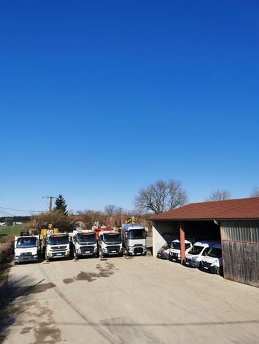 Des camions garés en rang par une journée ensoleillée, à côté d'un petit hangar en bois et d'arbres.
