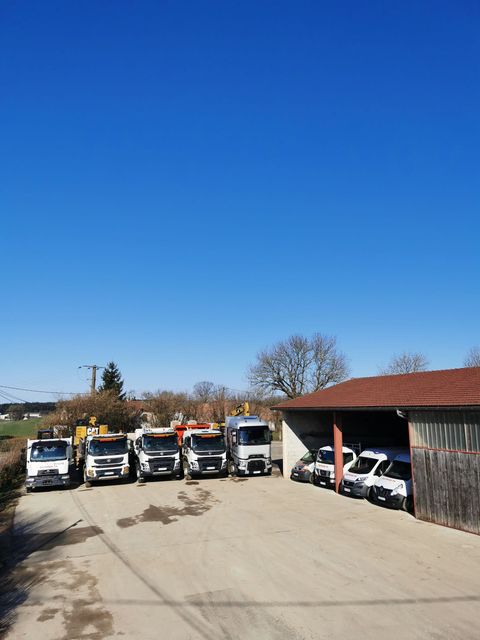 Des camions garés en rang par une journée ensoleillée, à côté d'un petit hangar en bois et d'arbres.