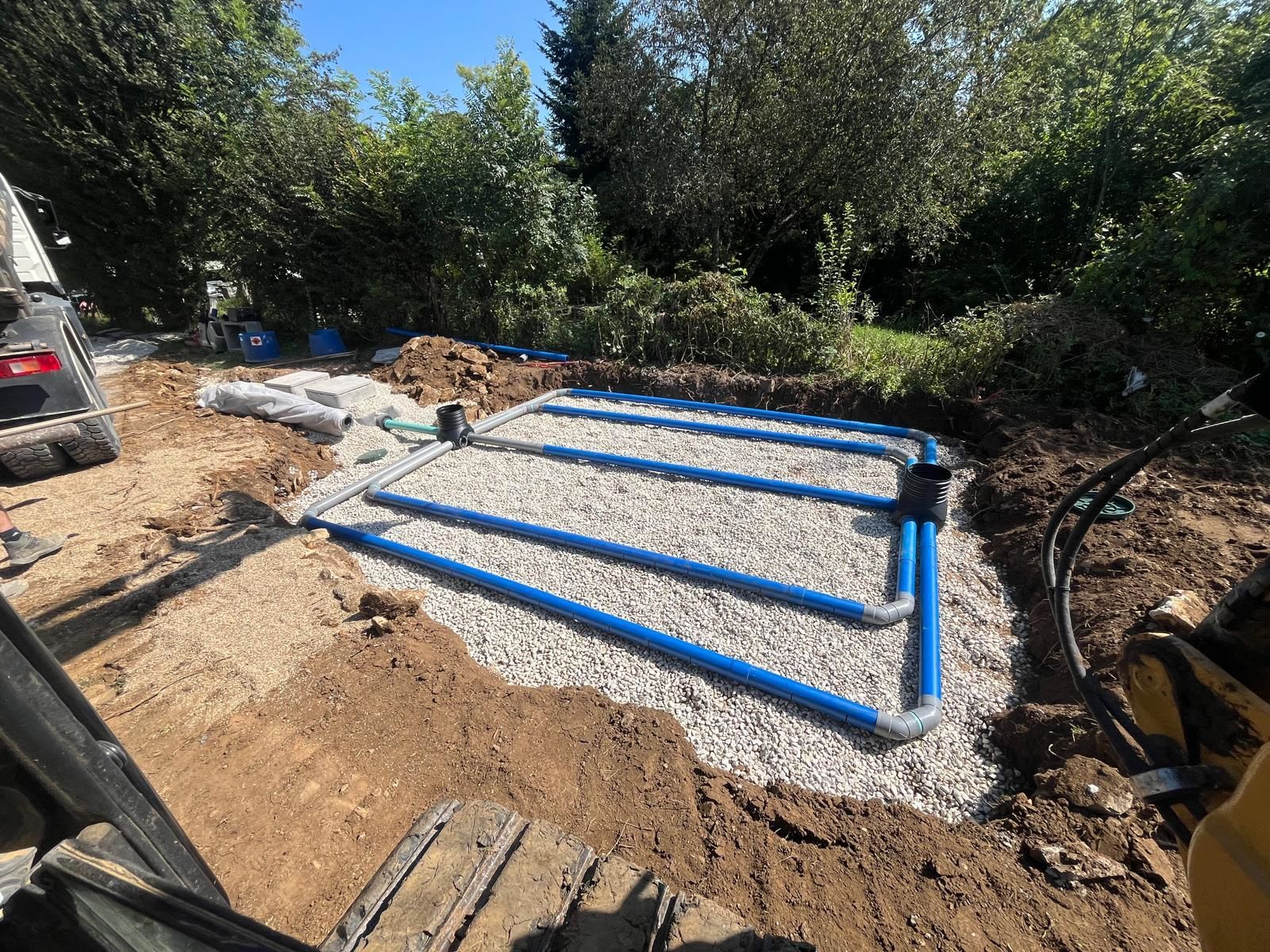 Tuyaux bleus dans du gravier dans une zone creusée, faisant partie d'une installation de système septique.