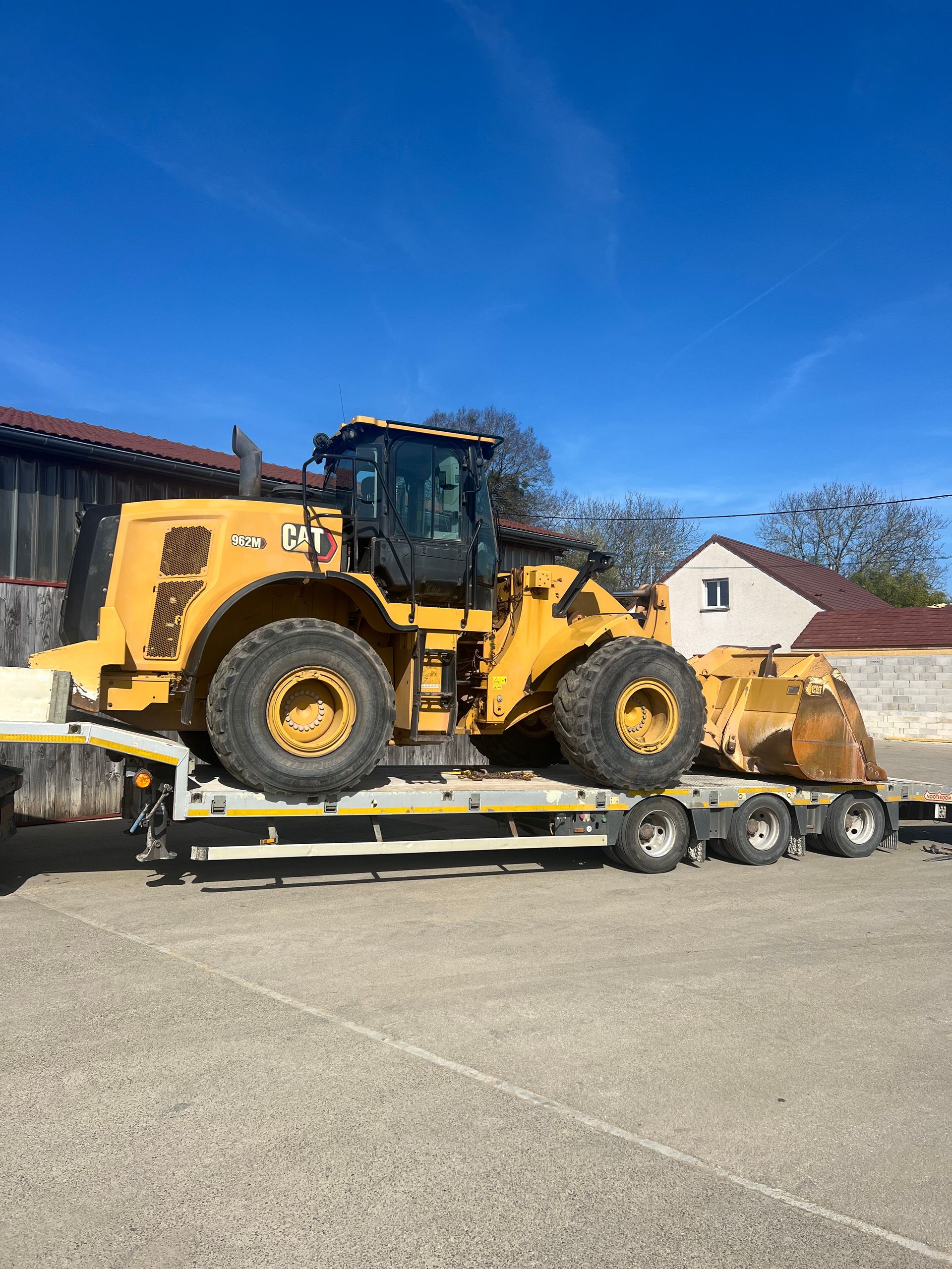 Chargeuse frontale jaune sur une remorque à plateau.
