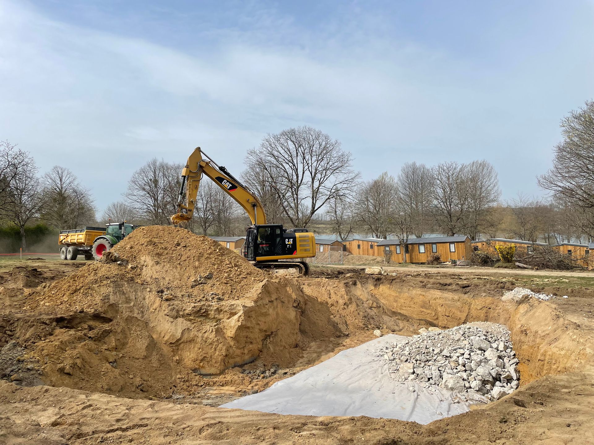 Une excavatrice creuse une grande fosse dans un espace ouvert. Un tas de débris s'y trouve.
