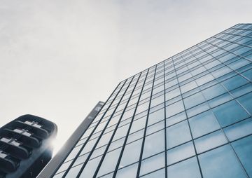 Edificio de oficinas de cristal visto desde abajo junto a una torre oscura y curva contra un cielo nublado.