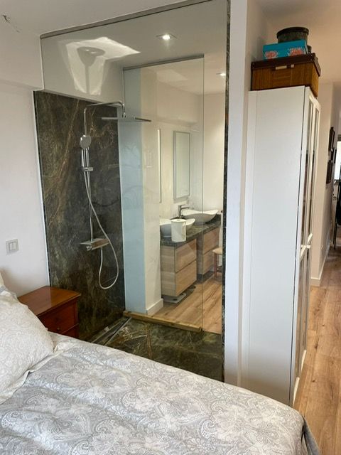 Dormitorio con ducha a ras de suelo, mampara de cristal y tocador en un espacio moderno y compacto.