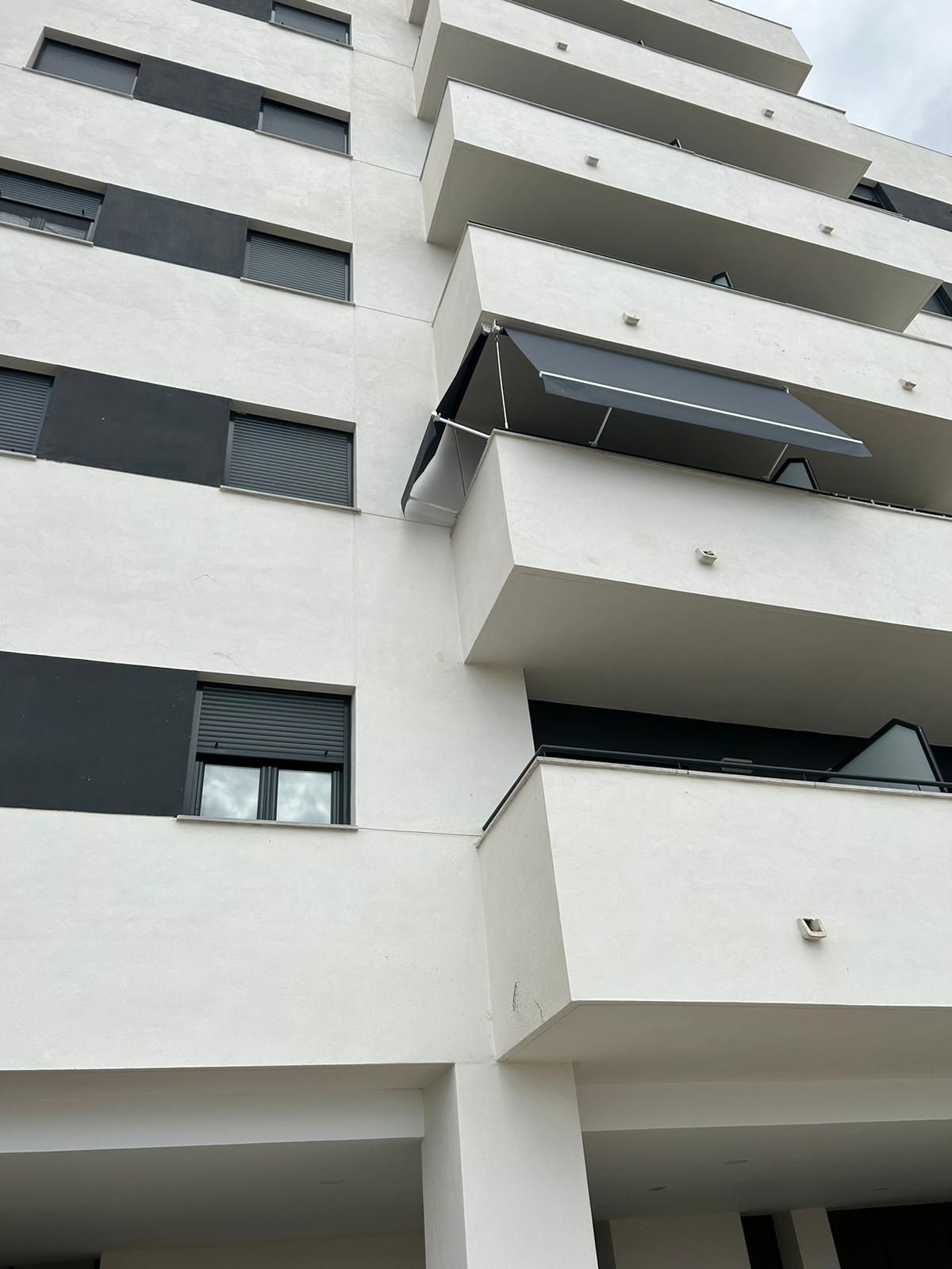 Edificio de apartamentos alto y blanco con balcones y contraventanas oscuras visto desde abajo