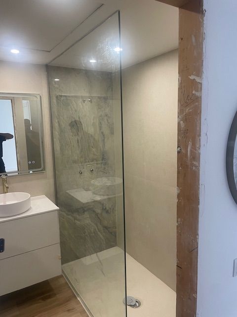 Baño moderno con ducha de cristal, tocador blanco y detalles de azulejos grises.