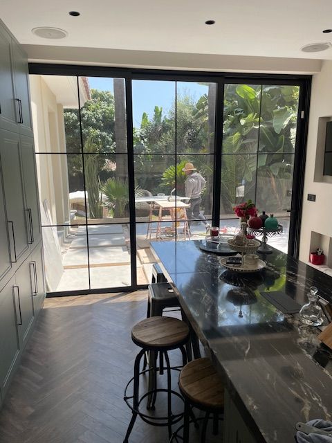 Cocina moderna y luminosa con isla con taburetes, puertas correderas abiertas y vistas al patio a través del cristal.