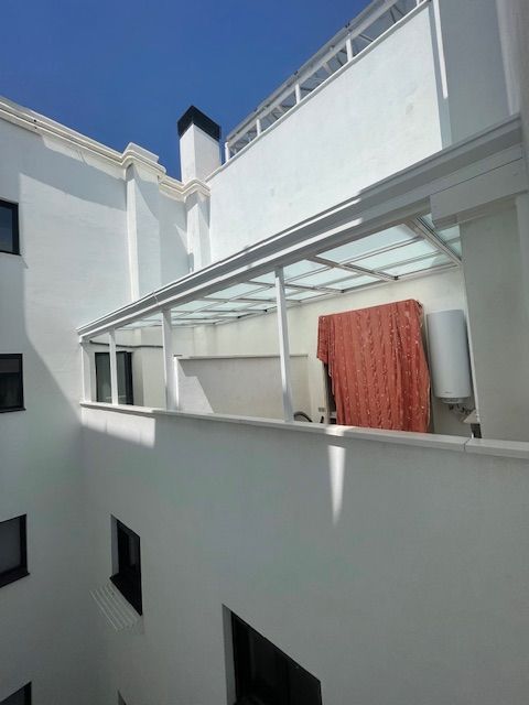 Patio interior de un apartamento blanco con balcones, ventanas y una toalla roja colgada en una terraza cubierta.