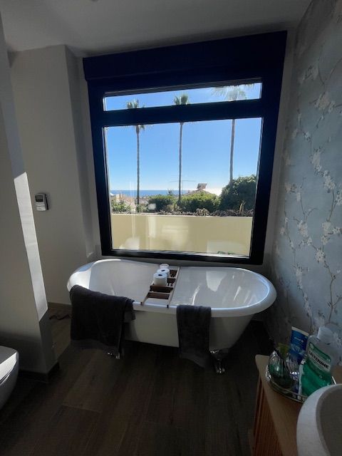Baño moderno con una bañera profunda junto a un gran ventanal con vistas al océano.