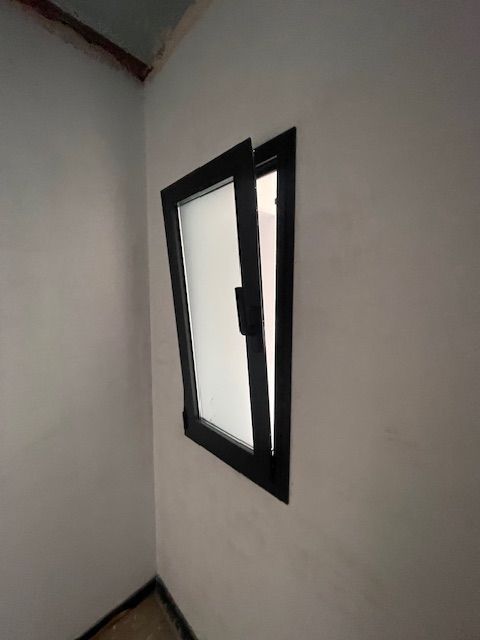 Ventana abierta con marco negro en una habitación de esquina blanca y desnuda con suelo oscuro.