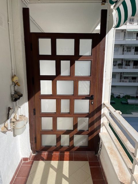Estrecho pasillo con balcón, rejado con celosía de madera y barandillas, con vistas a los apartamentos vecinos.