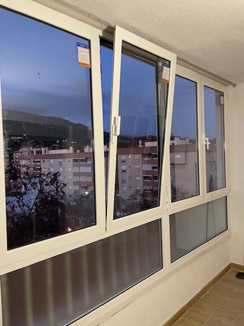 Ventana blanca abierta con vistas a edificios de apartamentos al anochecer.