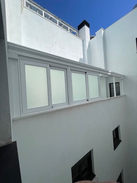 Patio de un edificio blanco con ventanas apiladas y un cielo azul arriba.