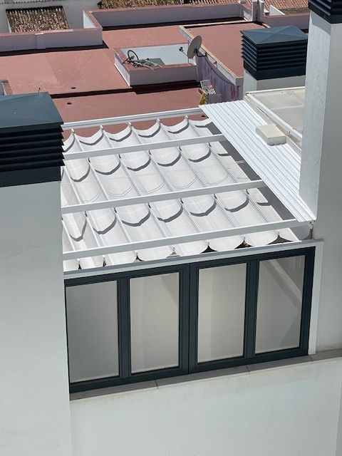 Azotea con toldo de tejas blancas y ventanas con marcos oscuros junto a los edificios vecinos.