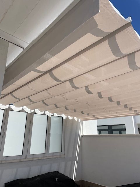 Toldo retráctil blanco sobre un balcón con paneles de vidrio esmerilado y una silla negra debajo.
