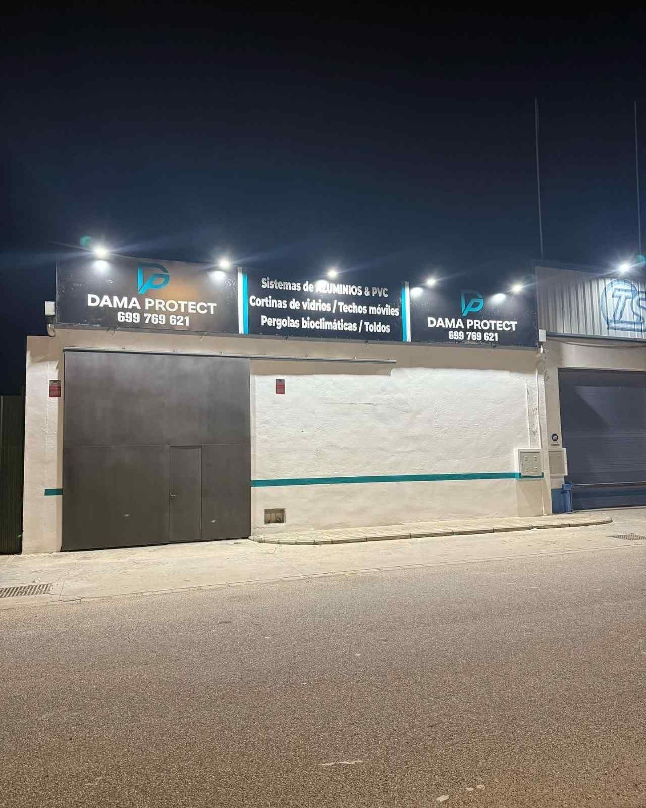 Vista nocturna de un local comercial cerrado con letreros iluminados y una puerta metálica en una calle tranquila.