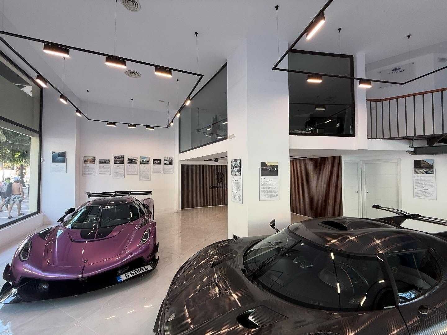 Dos coches deportivos en una moderna sala de exposición, uno morado y otro negro, bajo una brillante iluminación cenital.