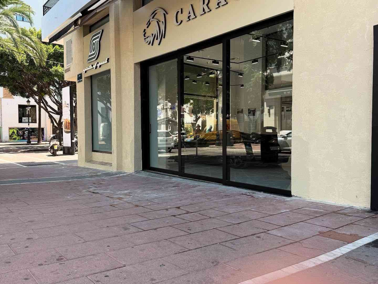 Fachada de cafetería con ventanas de cristal y acera de ladrillo en una soleada esquina.
