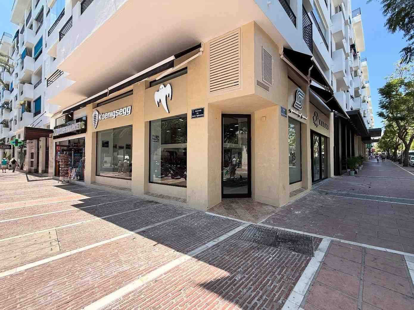 Local comercial en esquina en una soleada calle peatonal junto a un edificio de apartamentos de color beige.