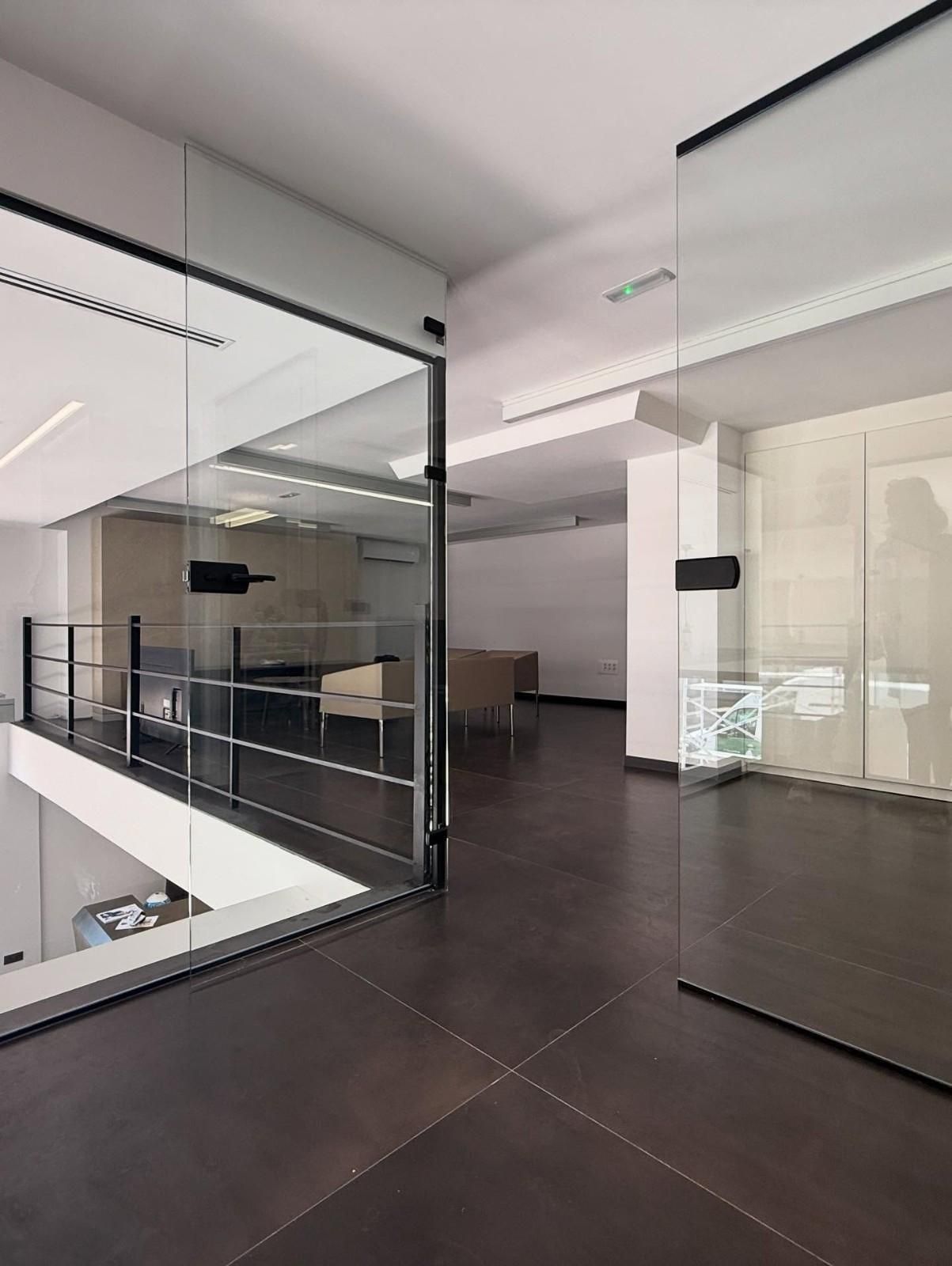 Interior de oficina moderno con barandillas de cristal, suelo de baldosas oscuras y pasillo abierto.
