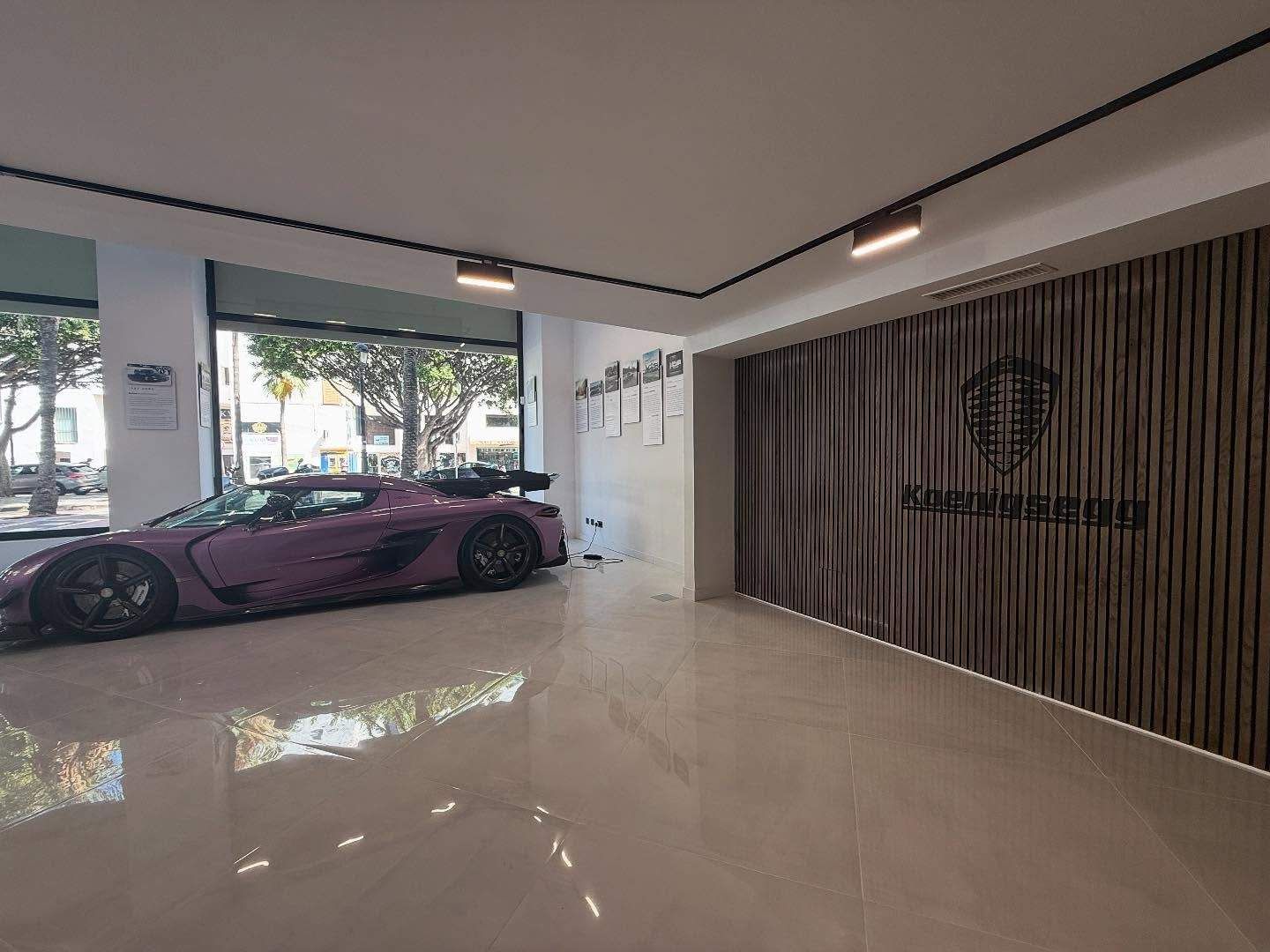 Moderna sala de exposición de garaje con un coche deportivo morado, suelo brillante y pared revestida de madera.