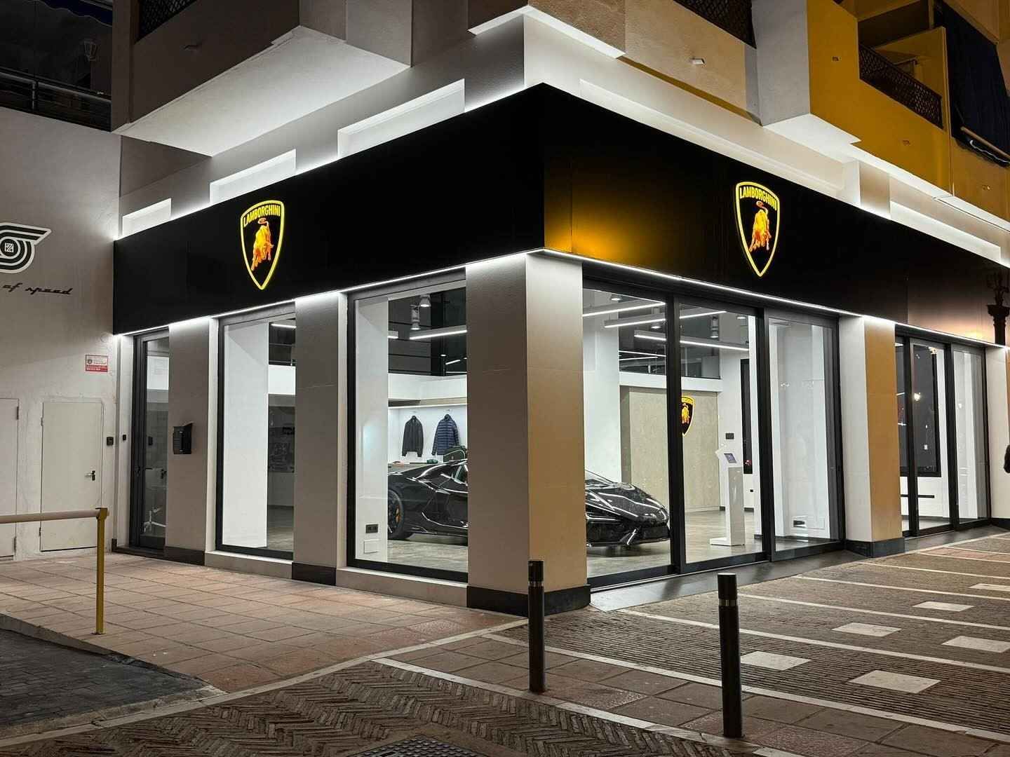 Rincón moderno de la sala de exposición de Lamborghini por la noche con letreros negros y dorados y ventanas de cristal.