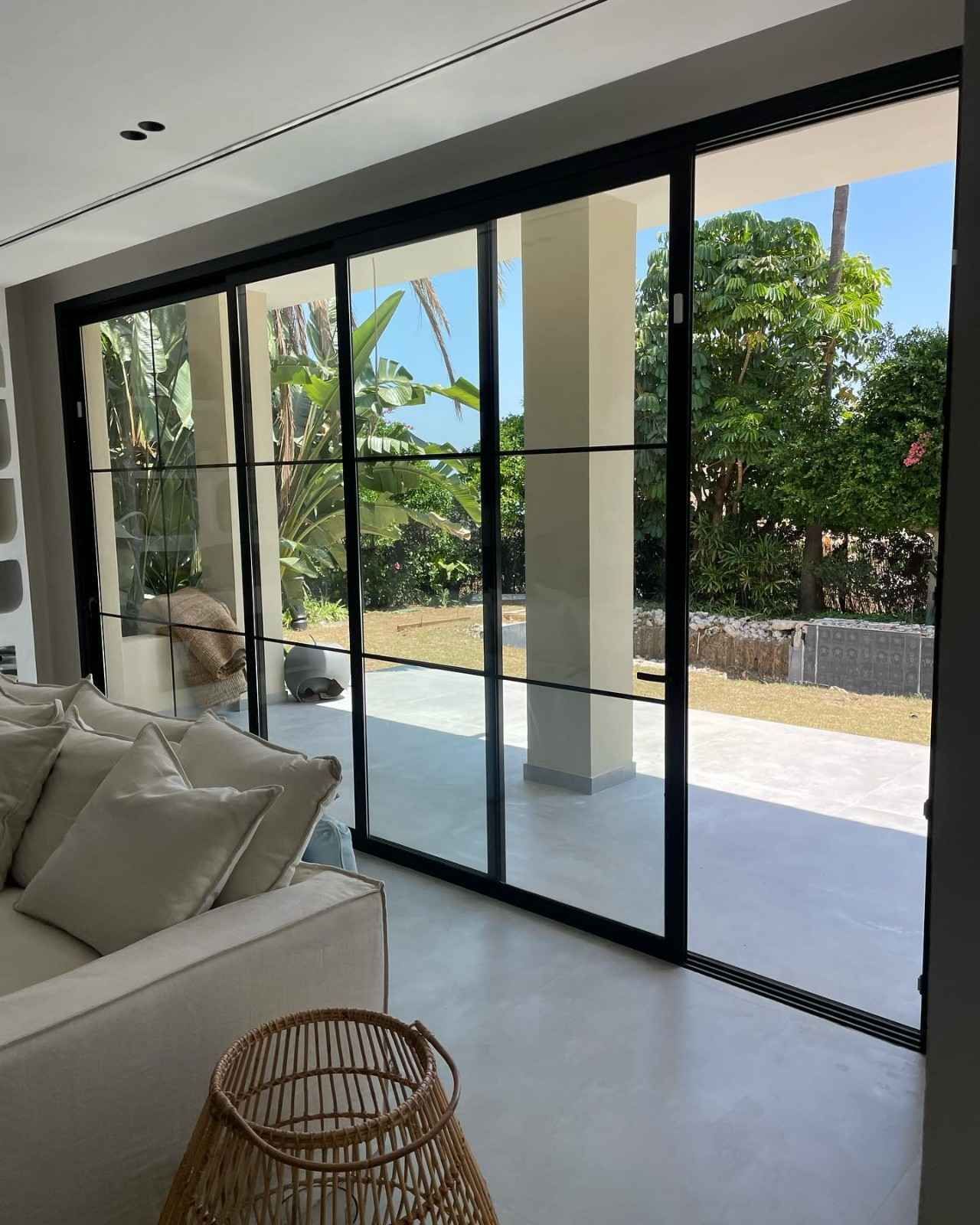 Salón moderno con puertas correderas de cristal que dan a un patio soleado y al jardín.