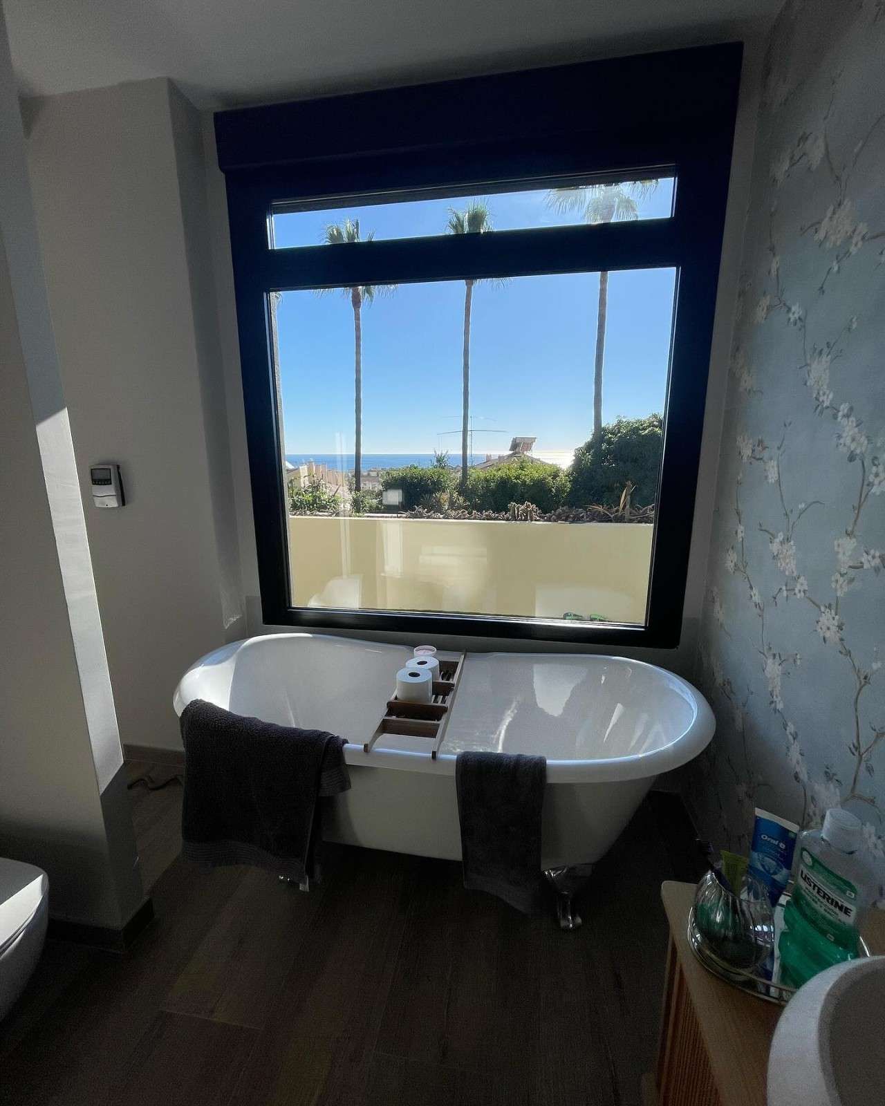 Baño moderno con bañera exenta junto a una ventana con vistas a la vegetación y al mar.