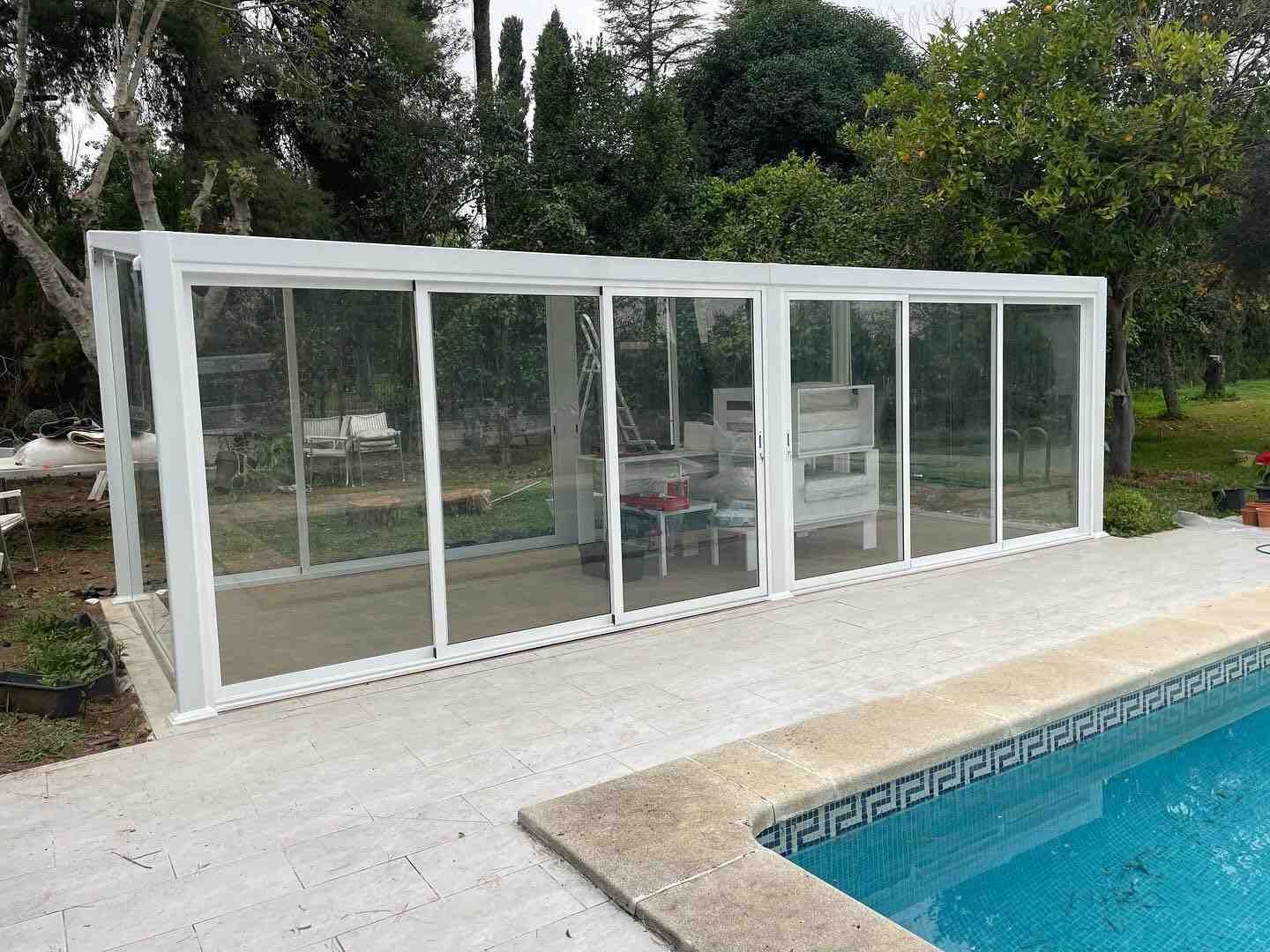 Estructura blanca acristalada junto a la piscina y el jardín trasero.