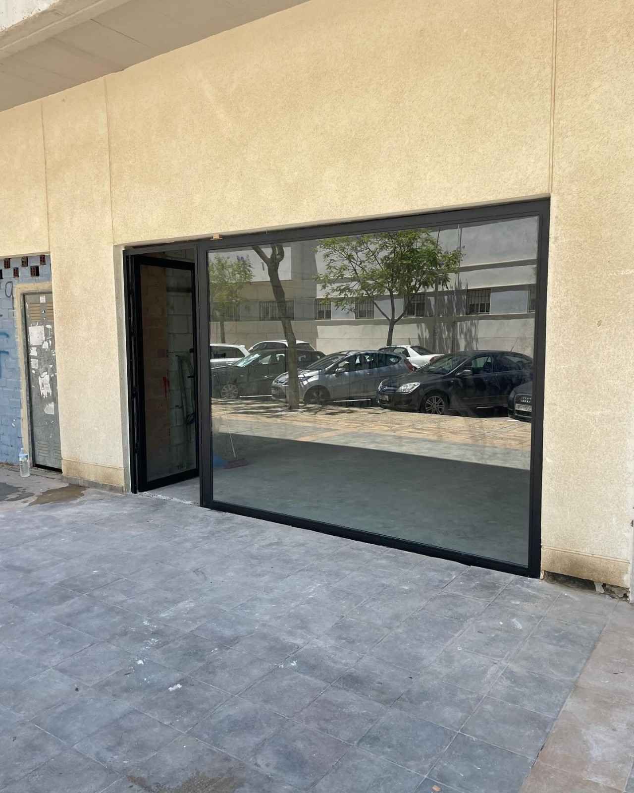 Local comercial vacío con un gran ventanal de cristal con marco negro y pared exterior de color beige.