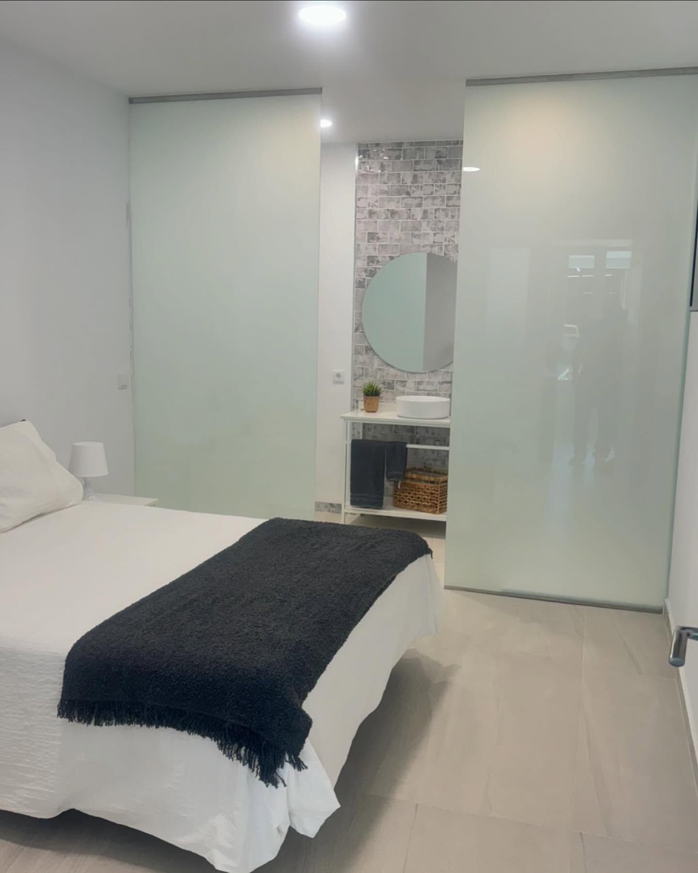 Habitación luminosa y moderna con armarios con puertas correderas, una cama y un pequeño tocador con espejo redondo.