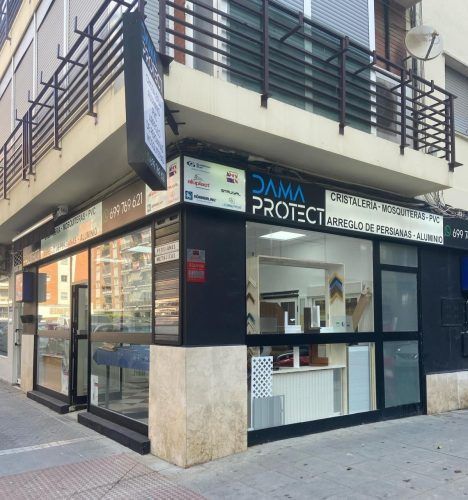Local comercial en esquina de “PMA Protect”, con ventanas de cristal y fachada beige y negra, situado en una calle de la ciudad.