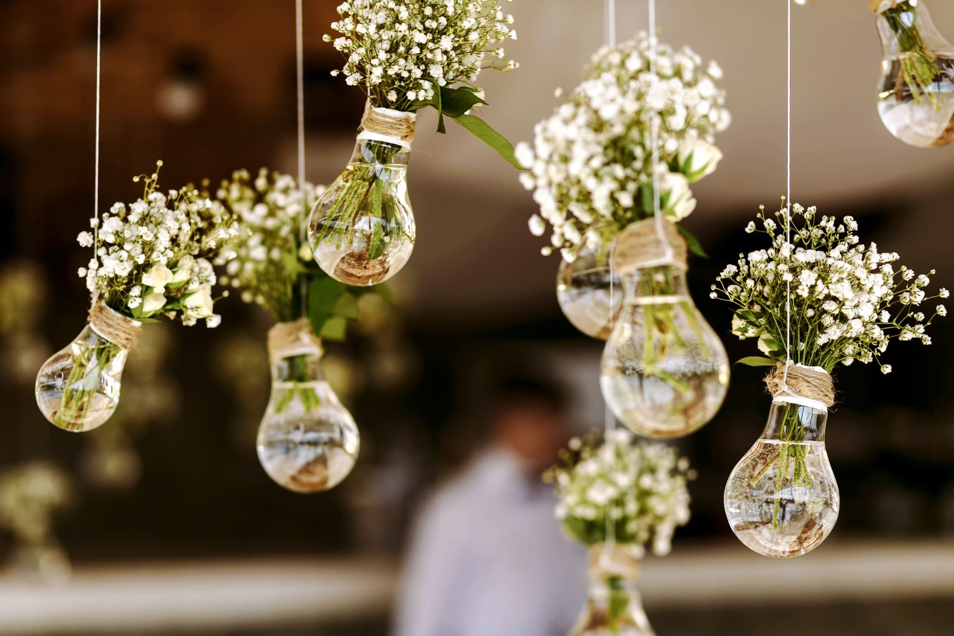 Des ampoules suspendues remplies de fleurs blanches sur un fond flou d'événement intérieur.
