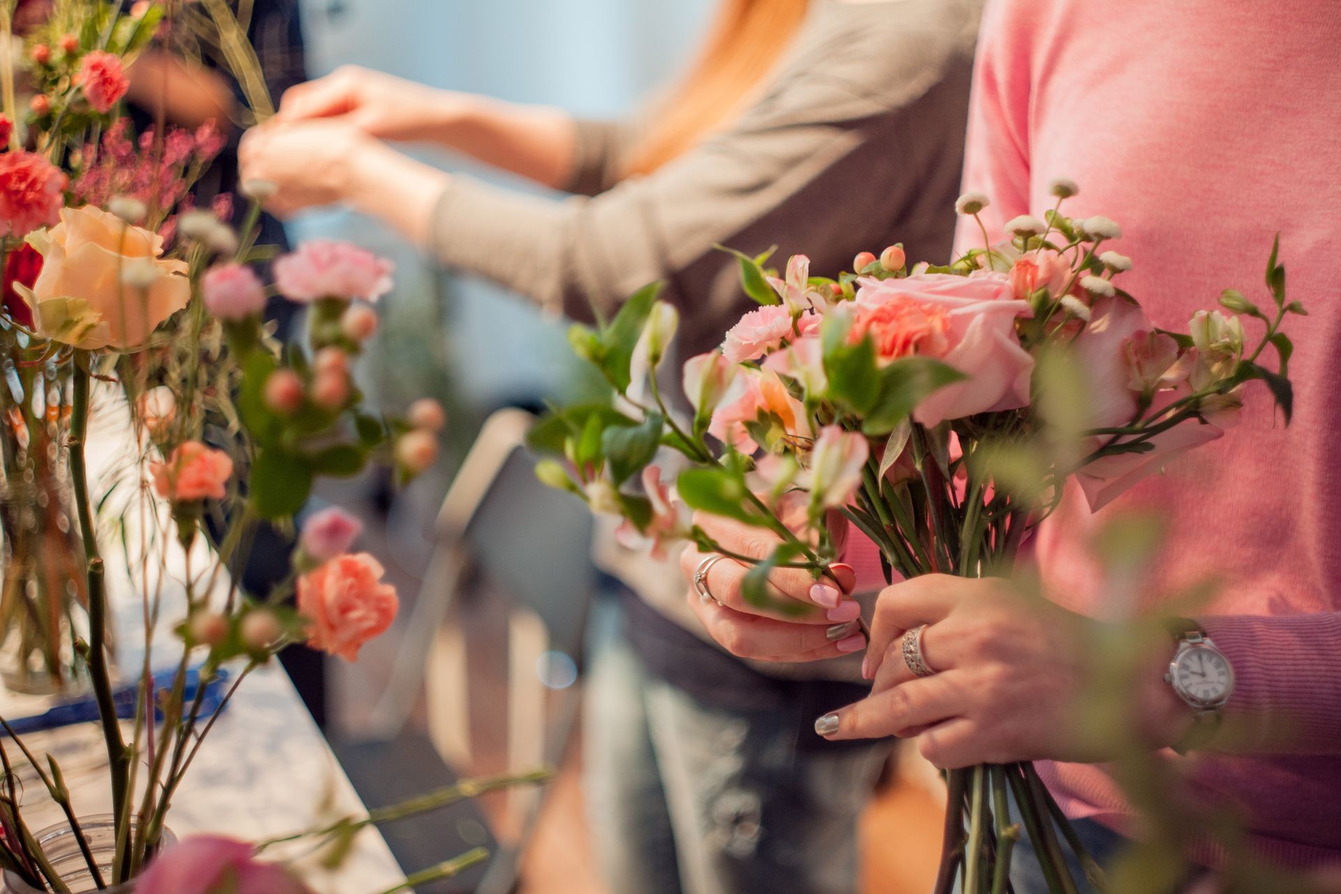 Des personnes arrangent des fleurs roses et pêche dans une boutique de bouquets.