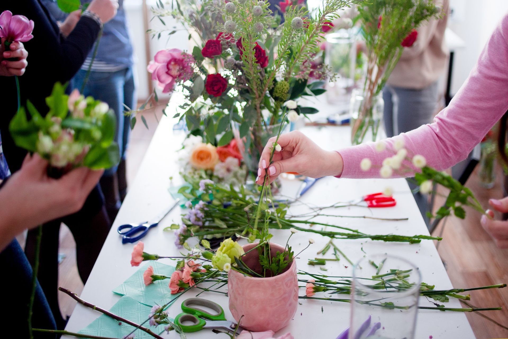 Des personnes arrangent des fleurs et de la verdure sur une table lors d'un atelier floral.